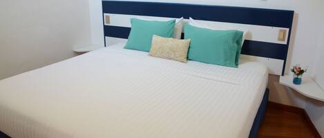 Una cama bien hecha con un cabecero blanco y azul, dos almohadas color turquesa y una almohada decorativa color beige.