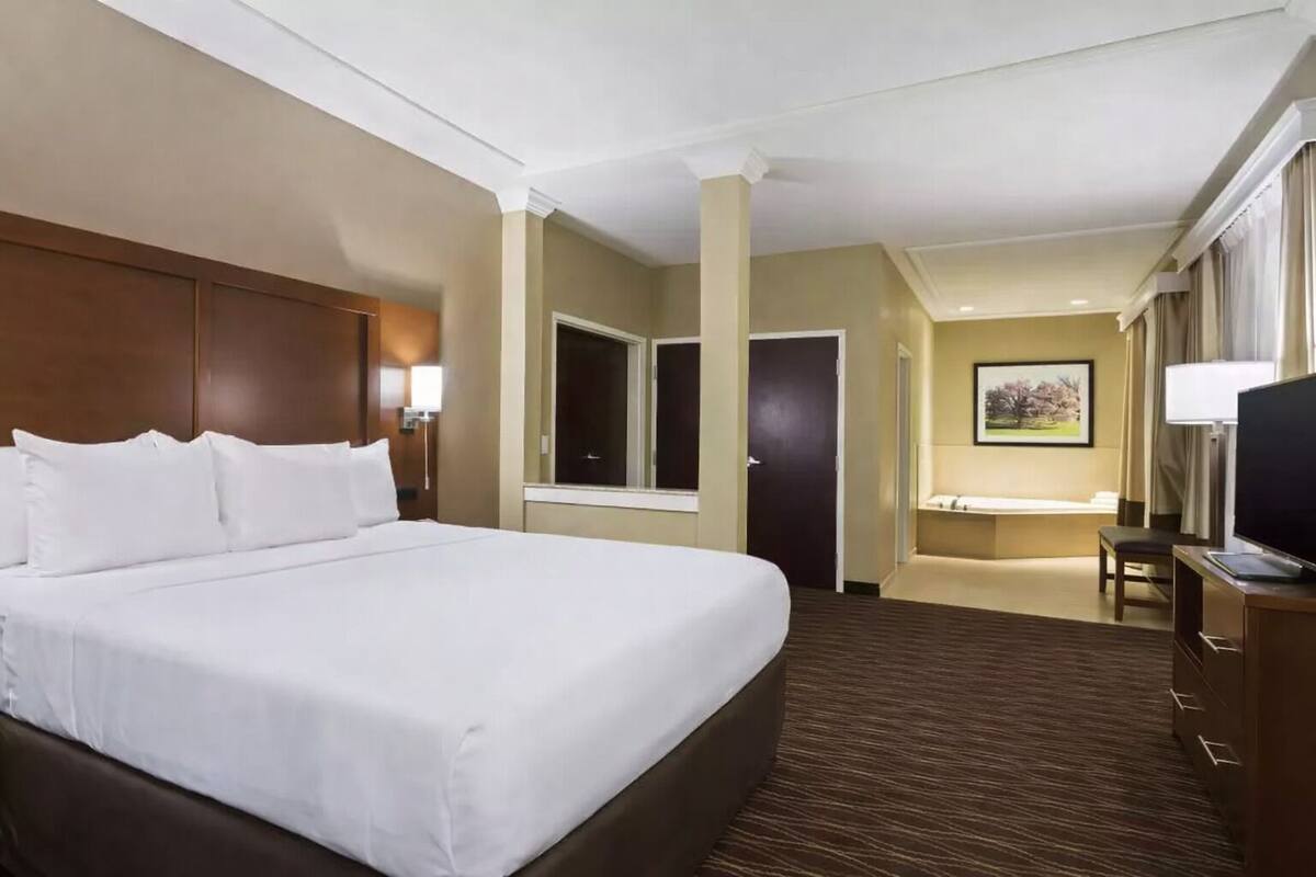 A hotel room with a large bed, a desk with a chair, a television, and a bathroom with a mirror and sink.