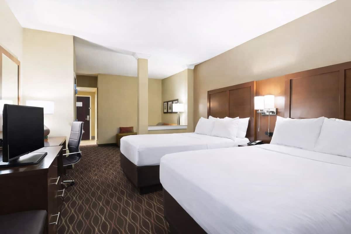 A hotel room with two beds, a desk, a TV, and a bathroom door.