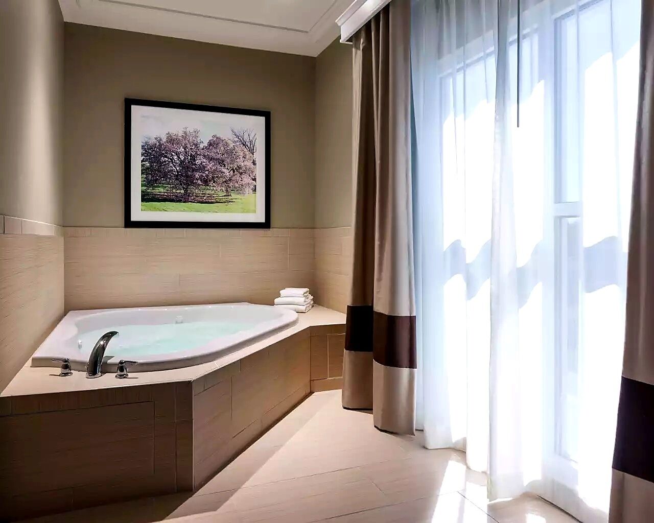 Een moderne badkamer met een ruime badkuip, een lijstwerk met een foto aan de muur en een raam met gordijnen.