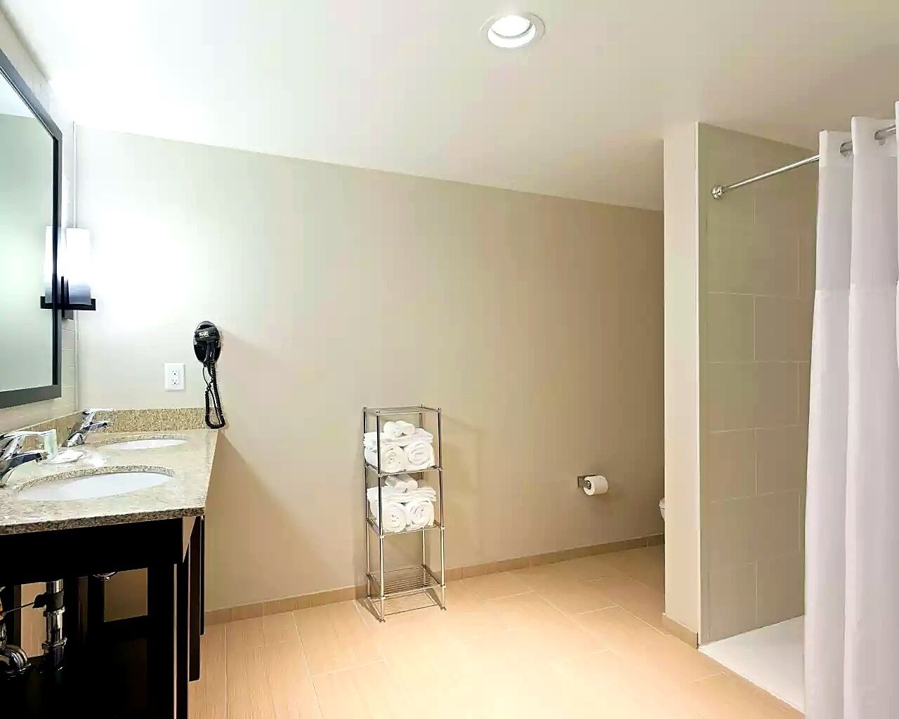 Une salle de bain avec deux lavabos, un porte-serviettes, un rideau de douche et des toilettes.