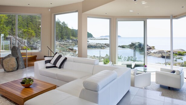 Una sala de estar moderna con un sofá blanco, una mesa de centro de madera y vistas a una costa rocosa a través de amplios ventanales.