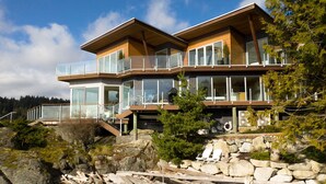 Una casa moderna de varios pisos con amplios ventanales, balcones de madera y base de piedra.