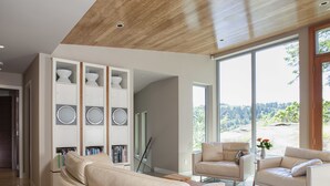 Una sala moderna con un sofá beige grande, dos sillones y una estantería empotrada con objetos decorativos.