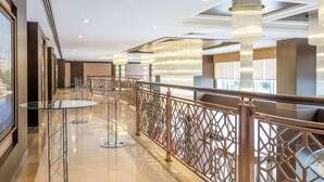 Un hall d’hôtel moderne avec des tables en verre, une rambarde décorative et des lustres suspendus.