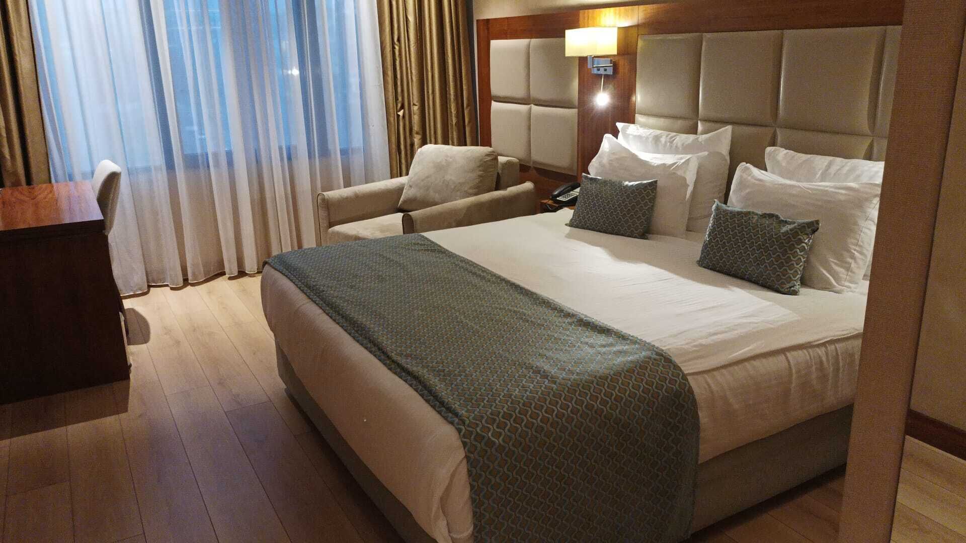 Habitación de hotel con una cama grande, una silla, un escritorio y una ventana con cortinas.