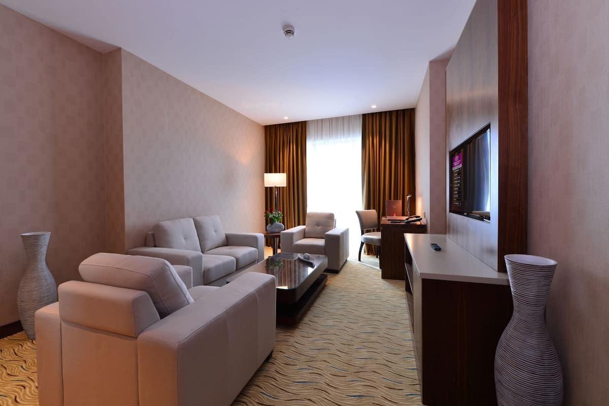 A hotel room with a sofa set, a coffee table, a TV, and a desk.