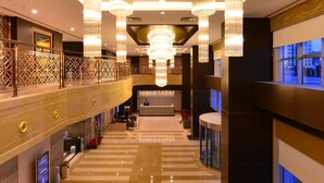 Un hall d’entrée spacieux avec un comptoir d’enregistrement, des espaces de détente et de grands lustres.