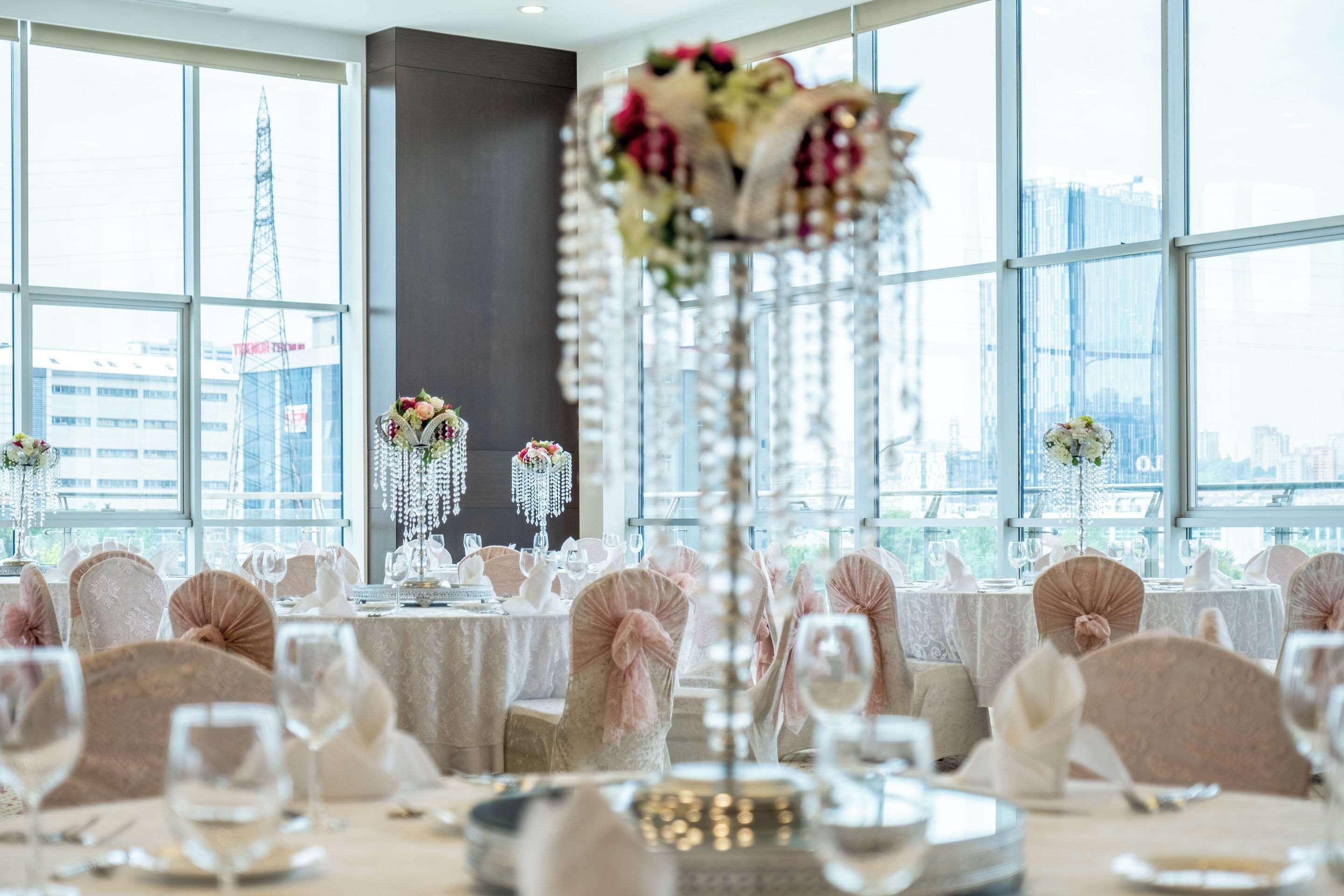 Un salón de banquetes con mesas dispuestas para un evento formal, ventanas amplias y vistas a la ciudad.
