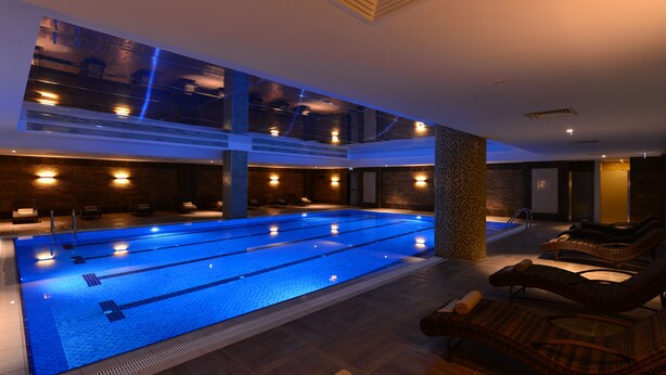 Une piscine intérieure moderne dotée de plusieurs couloirs de nage, de chaises longues et d’un toit en verre.