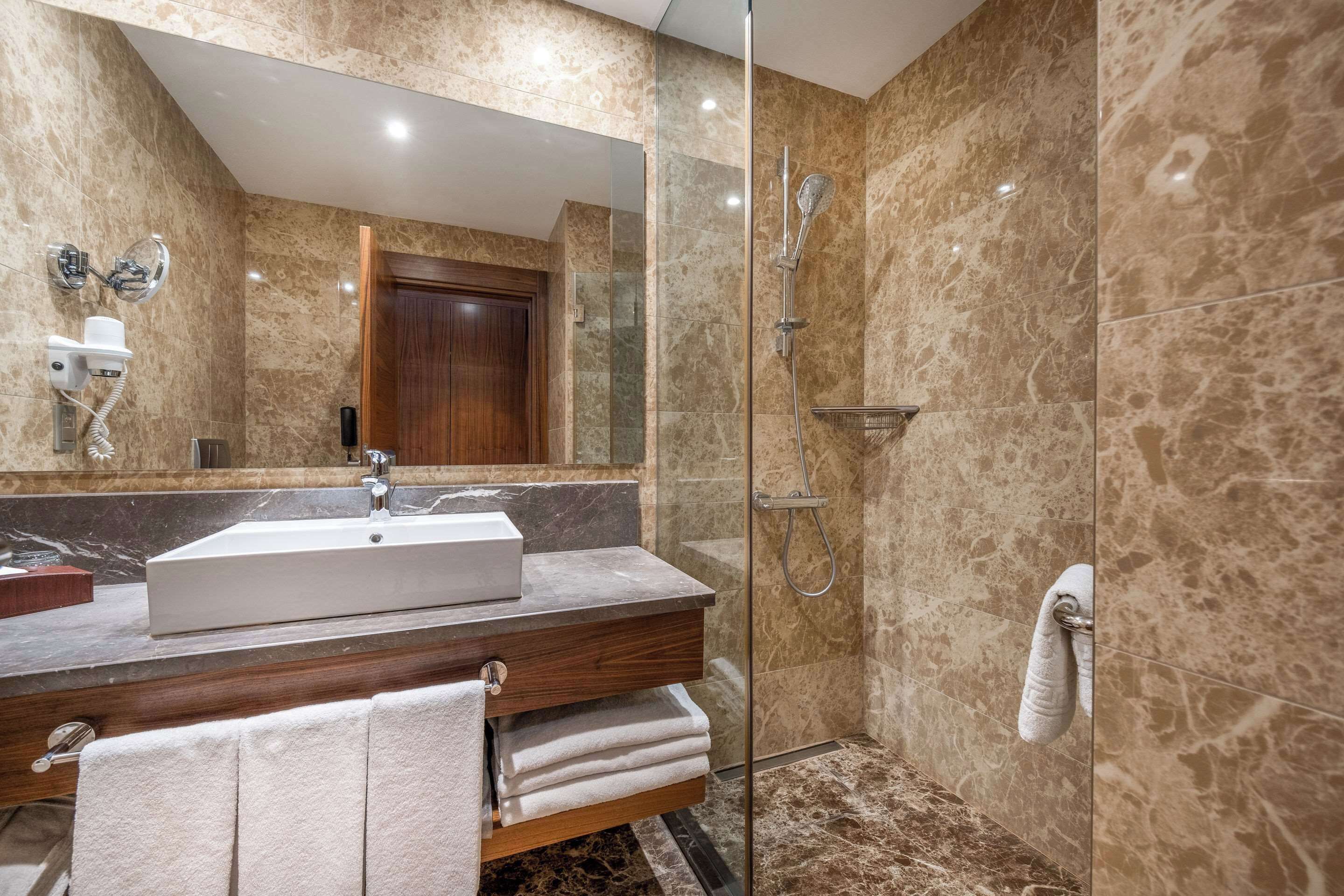 Une salle de bain moderne avec un grand miroir, un lavabo, une douche et des murs en marbre.