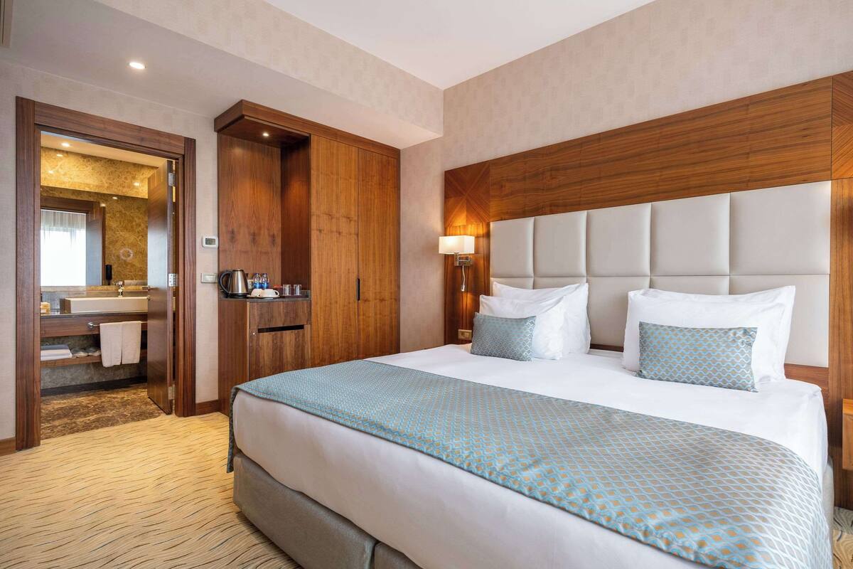 A hotel room with a large bed, wooden headboard, and a bathroom visible through an open door.
