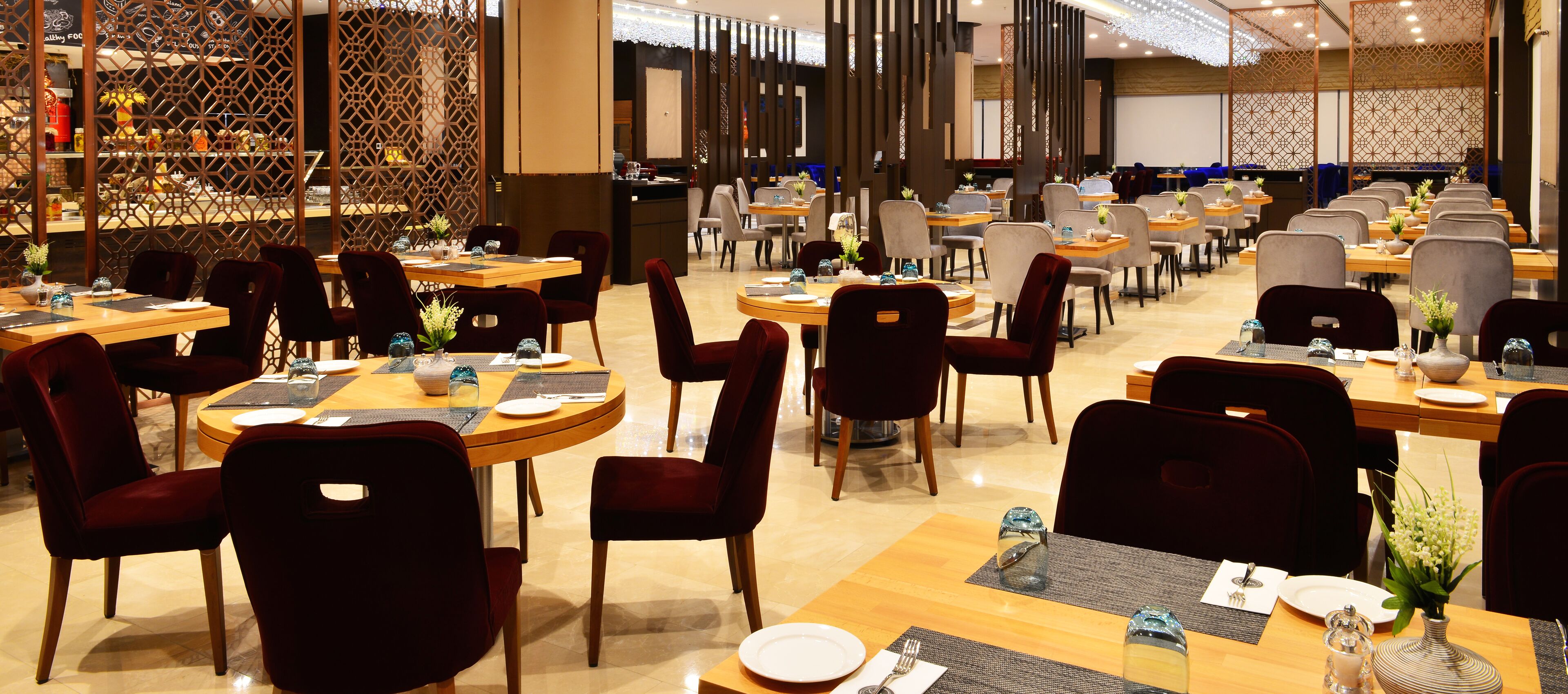 Een ruime restaurantruimte met meerdere eettafels en stoelen, een decoratieve scheiding en een goed verlicht interieur.