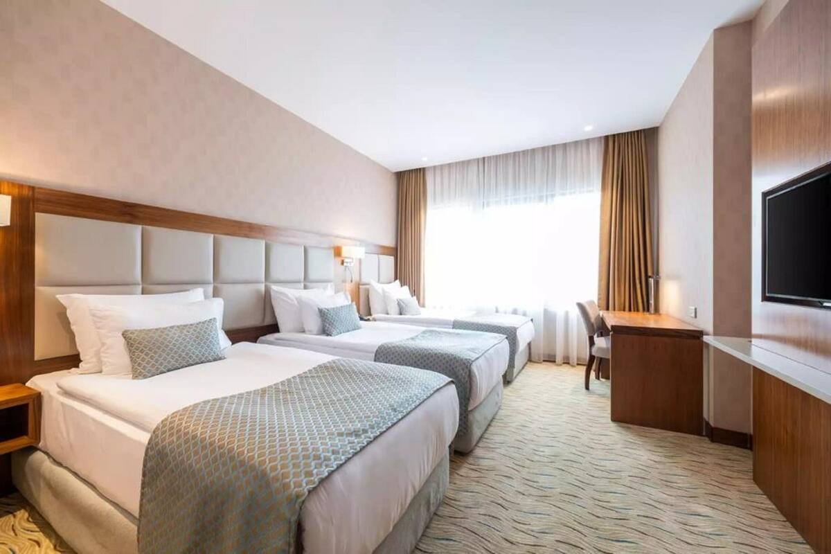 A hotel room with three beds, a desk, and a television.