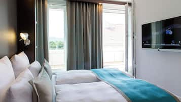 A hotel room with a bed, a TV mounted on the wall, and a window with curtains.