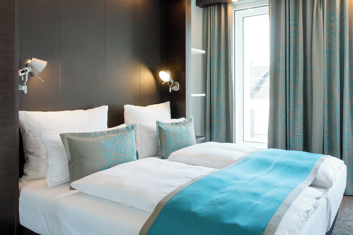 A hotel room with a large bed, two wall-mounted lamps, and a view of the outdoors through the window.