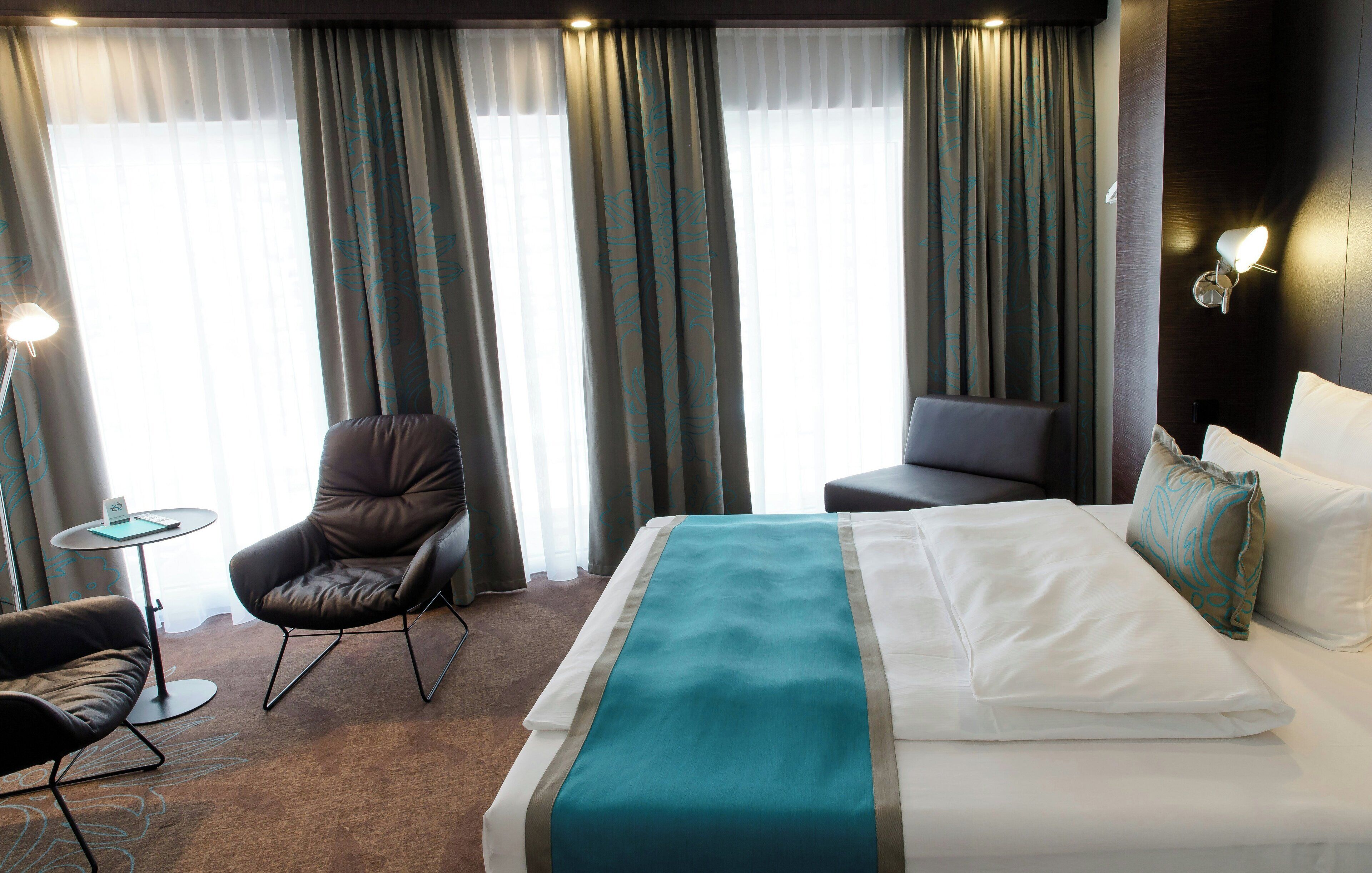 A hotel room with a bed, two armchairs, a small table, and a lamp.