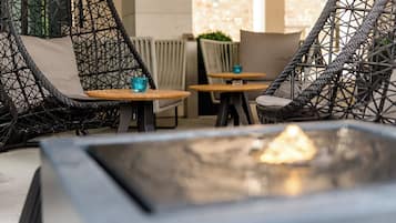 A cozy outdoor seating area with wicker chairs and tables, a fire feature, and a view of the building's exterior.