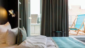 Habitación de hotel con cama, almohadas, una ventana con cortinas, un balcón con una silla y una lámpara fijada a la pared.