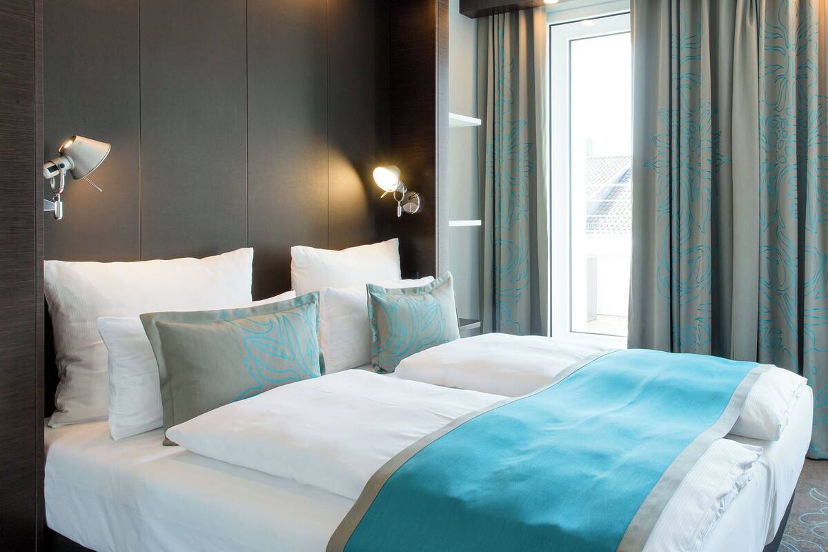 A hotel room with a large bed, two wall-mounted lamps, and a view of the outdoors through the window.