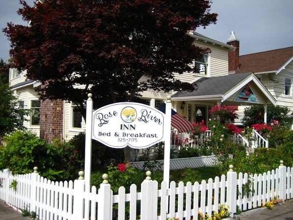 Placa do Rose River Bed & Breakfast, com cerca branca e vegetação exuberante.