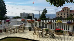 Um terraço com área de estar externa e plantas em vasos, com vista para uma paisagem urbana com edifícios e uma bandeira.
