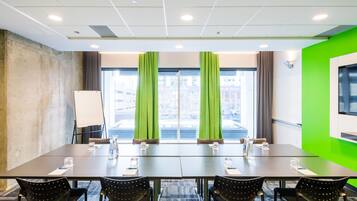 Un salón de conferencias con una larga mesa, cuatro sillas, una pizarra y un ventanal con cortinas.