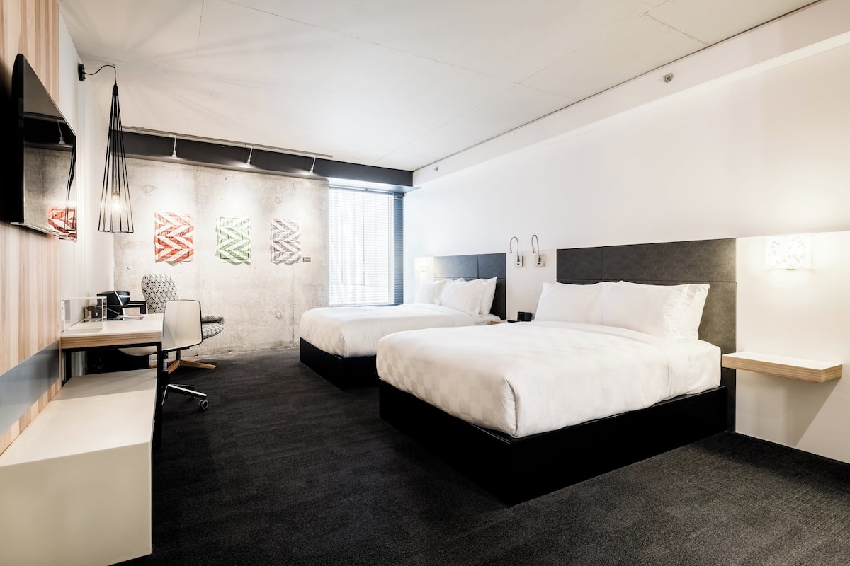 Ein modernes Hotelzimmer mit zwei Betten, einem Schreibtisch und einem großen Fenster.