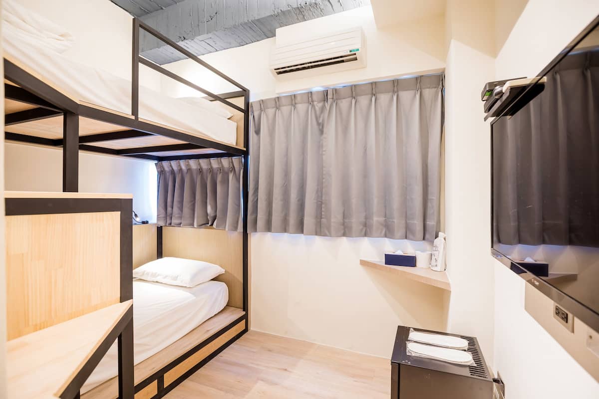 Habitación de hotel pequeña con una cama litera, un escritorio, un televisor y una ventana con cortinas.