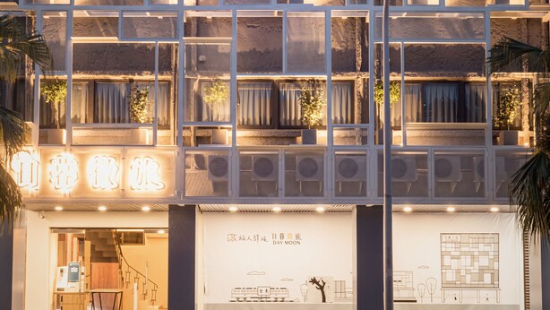 A multi-story hotel with a grid-like facade, balconies with potted plants, and a storefront with signage. - Traveller Inn Day Moon (Taitung)