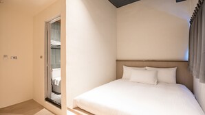 A bedroom with a large bed, a wooden headboard, and a sliding glass door leading to a bathroom. - Traveller Inn Day Moon (Taitung)