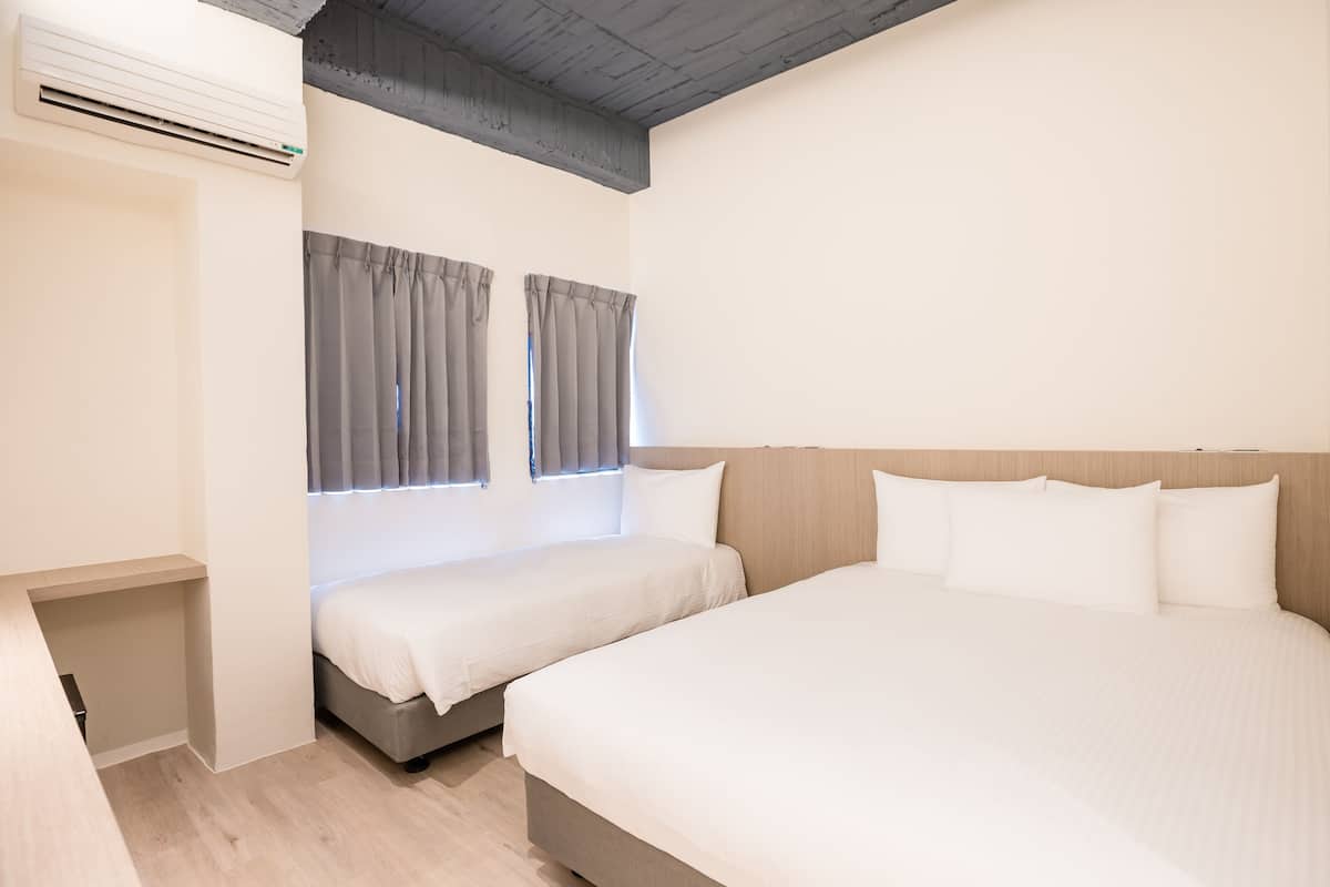 Habitación de hotel con dos camas, cabecero de madera, unidad de aire acondicionado integrada y una mesita de noche pequeña.