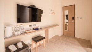 A modern hotel room with a flat-screen TV, a wooden bench, a small table with toiletries, and a wooden door. - Traveller Inn Day Moon (Taitung)