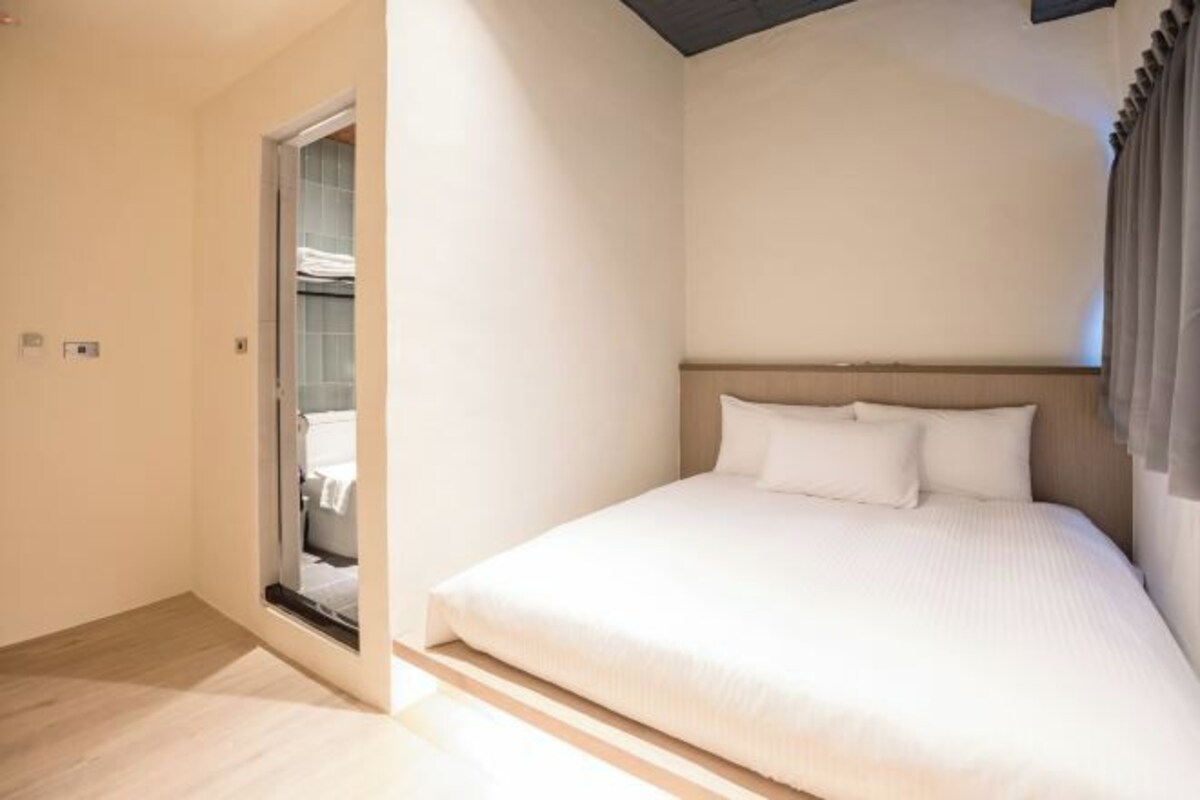 A bedroom with a bed, a window with curtains, and a door leading to a bathroom.