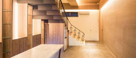 A modern interior with a wooden staircase, a long table, and a tiled floor.
