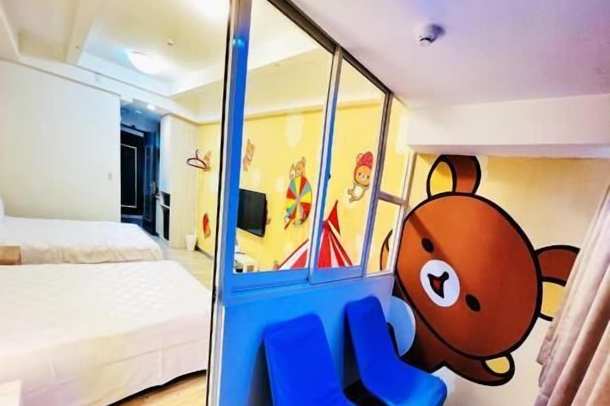 A hotel room with a bed, a blue seating area, and a bear mural on the wall.