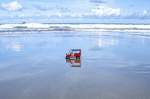 A red vehicle on a beach with a clear sky and ocean in the background.