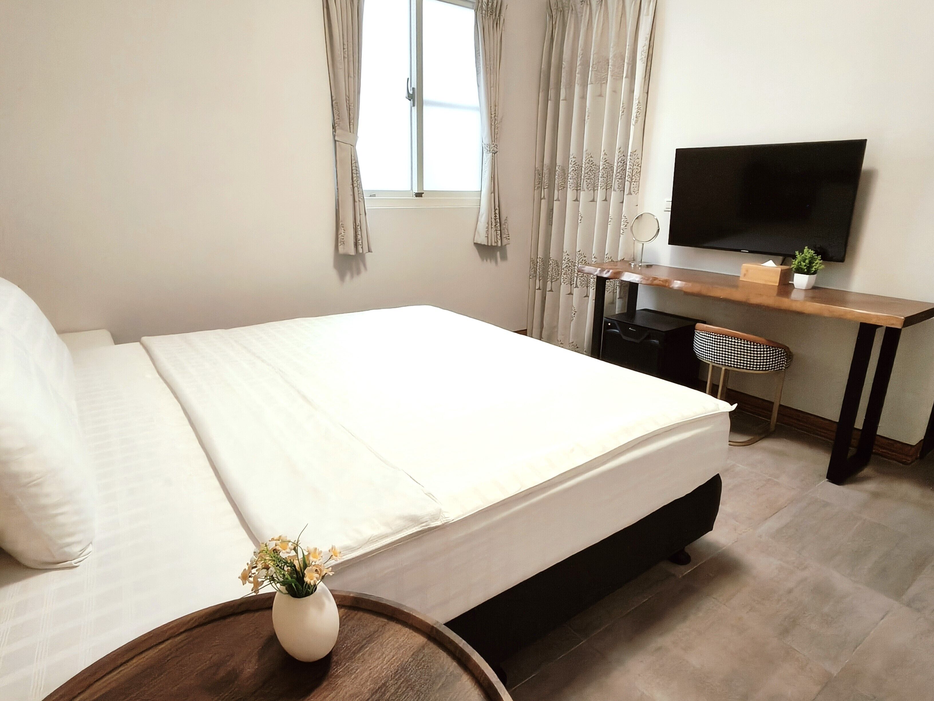 Ein Schlafzimmer mit Bett, Schreibtisch, Stuhl, Fernseher und einer kleinen Pflanze.