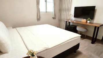 Ein Schlafzimmer mit Bett, Schreibtisch, Stuhl, Fernseher und einer kleinen Pflanze.