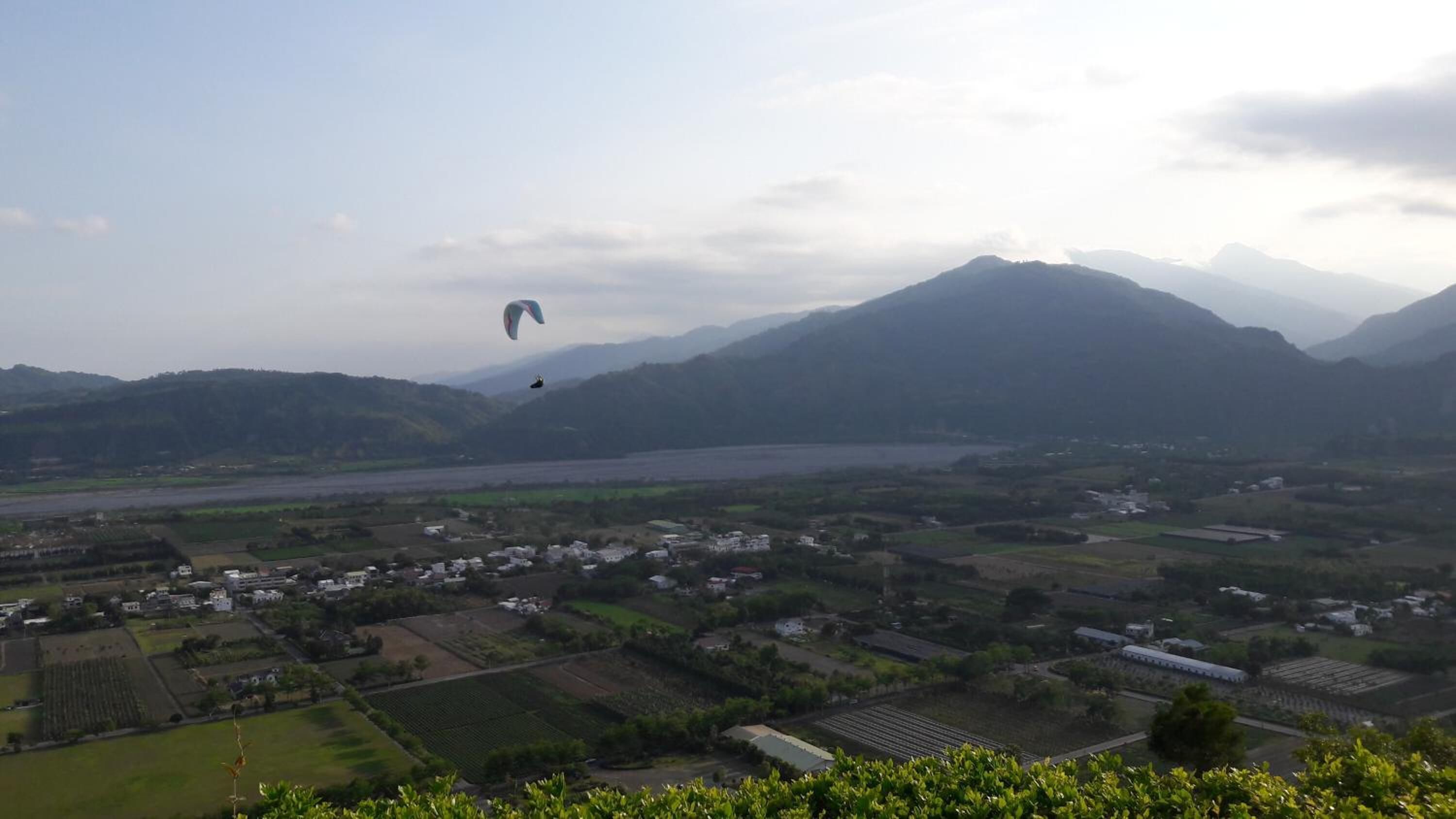 A rural landscape with fields, a river, and mountains in the background.