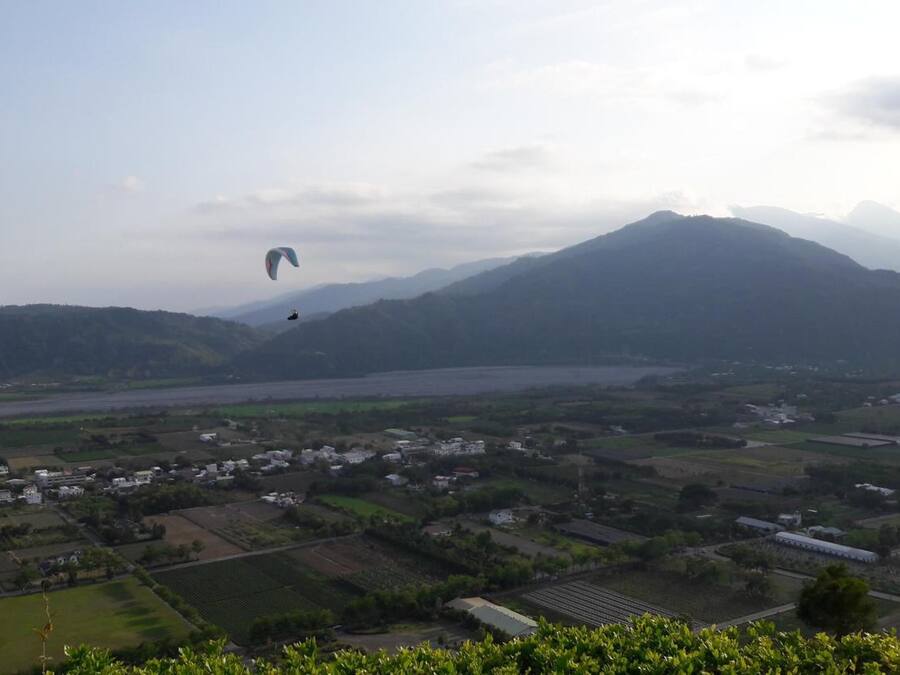 A rural landscape with fields, a river, and mountains in the background.