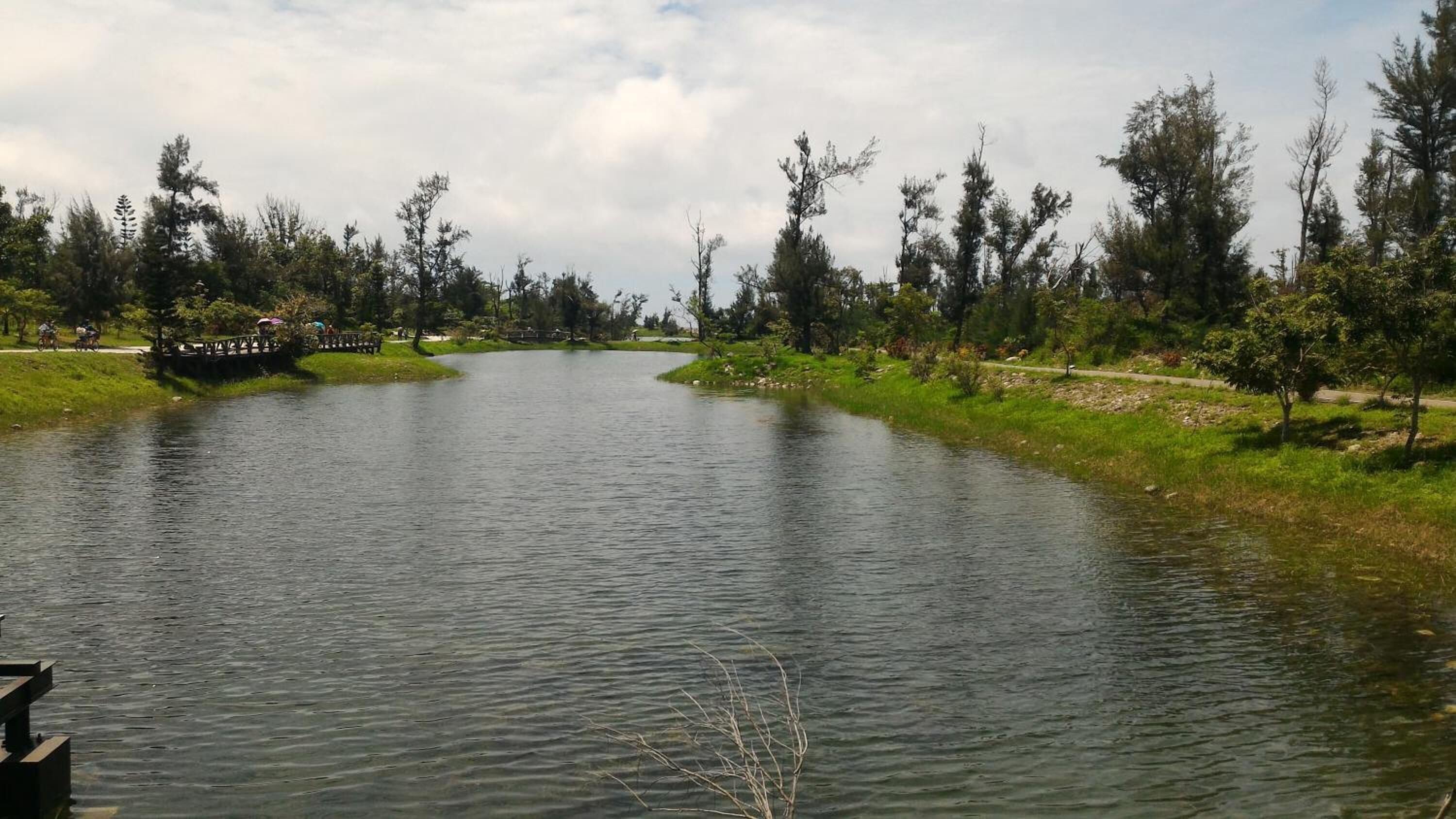 A calm river with a wooden dock and benches, surrounded by trees and grassy banks.