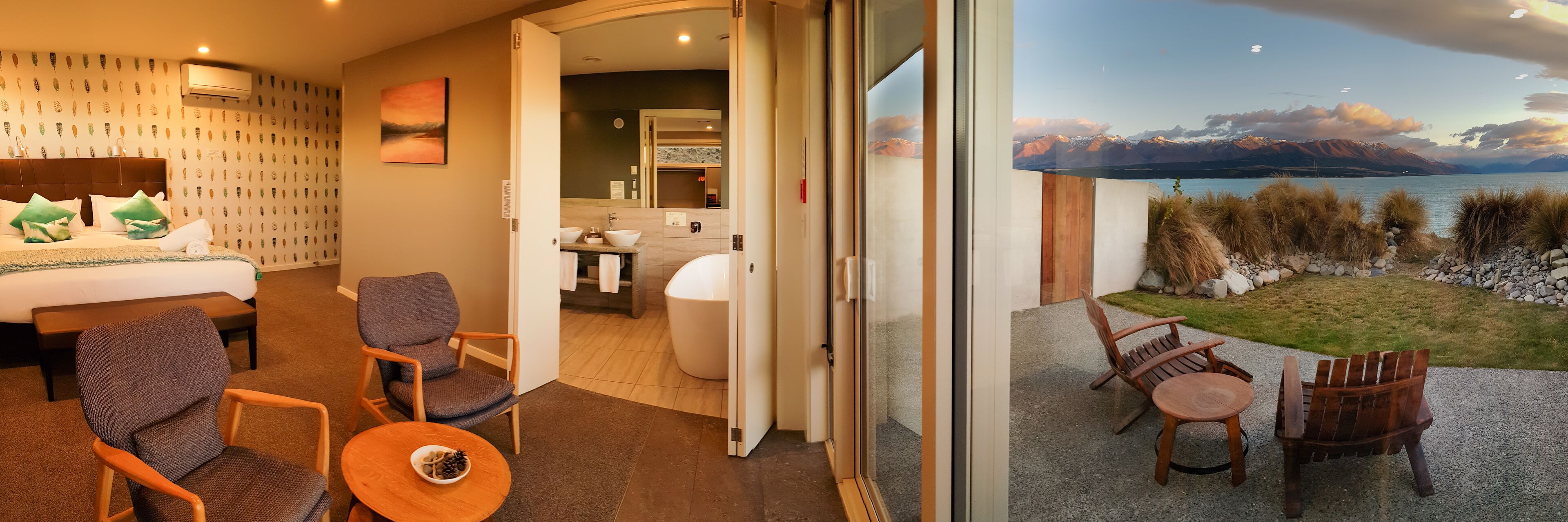 Quarto de hotel com cama, área de estar e vista para um lago e montanhas.