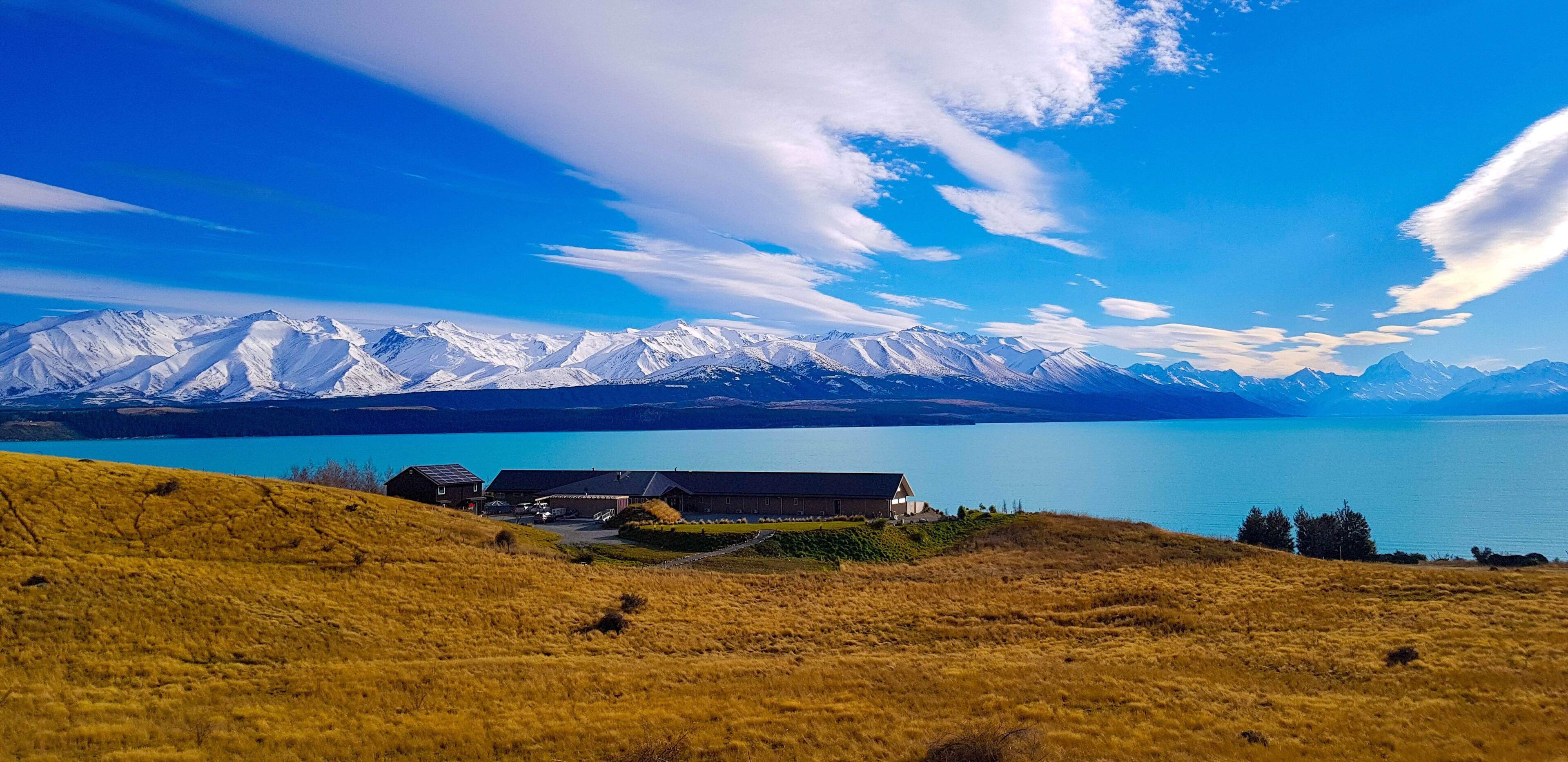 Un paisaje montañoso con un lago, un edificio de techo inclinado y un cielo despejado.