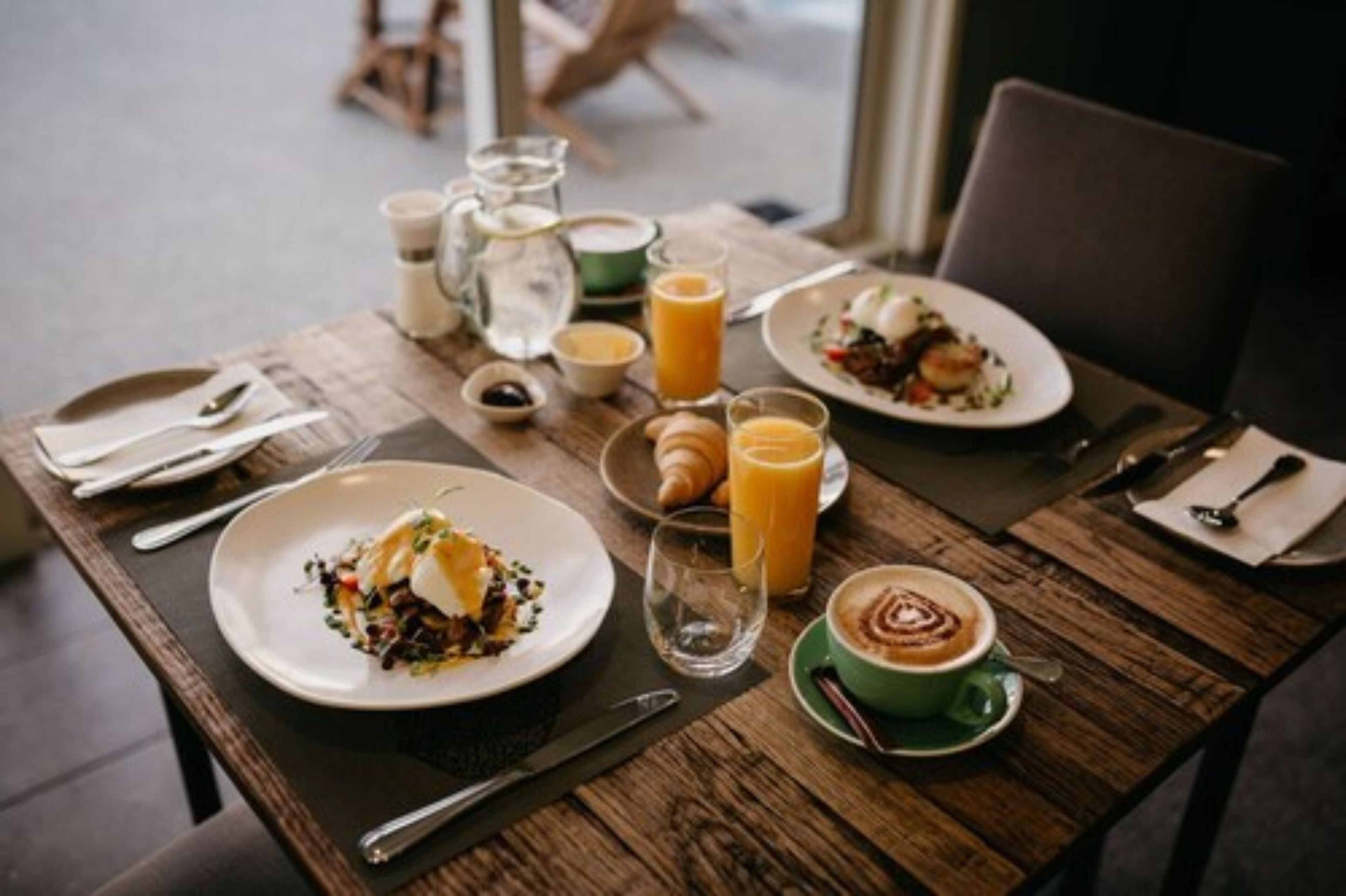 Una mesa de madera con platos de comida, una taza de café y un vaso de jugo de naranja.
