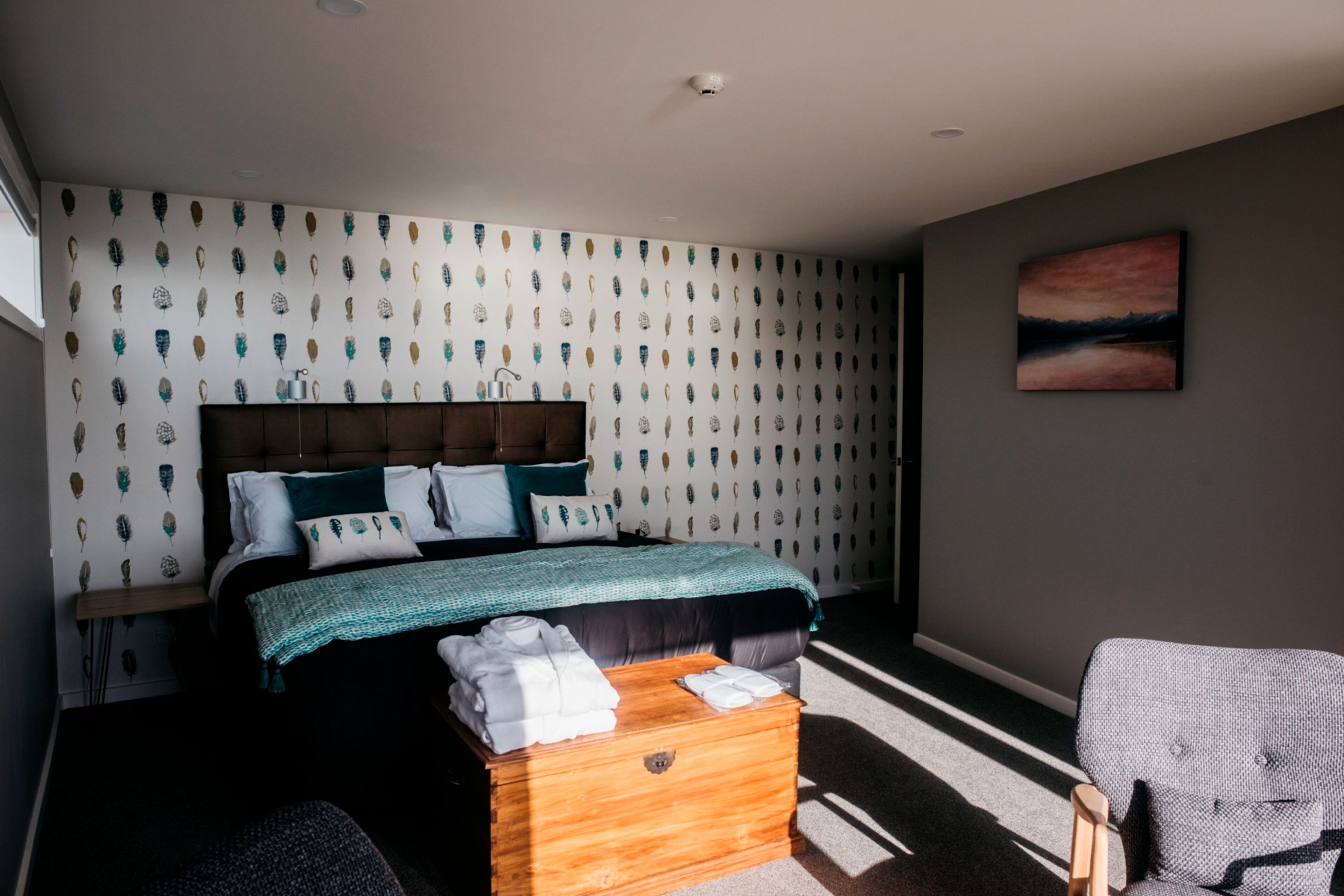A modern bedroom with a large bed, a wooden chest, and a chair.