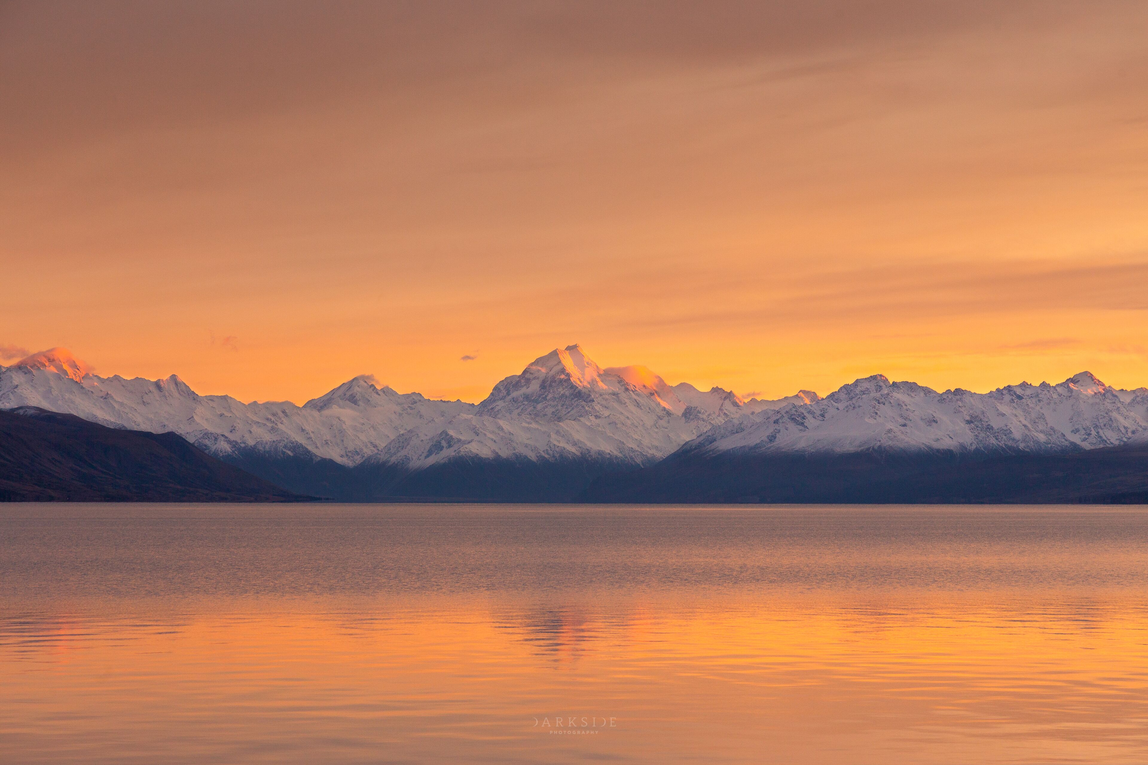 A mountain range reflected in a calm lake during sunset.