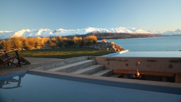 Zona de piscina con escalones que conducen a una terraza con vistas a un lago y montañas nevadas.