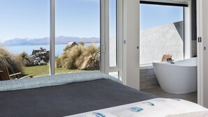 Un dormitorio con una cama grande, una bañera y vistas a montañas y al agua.