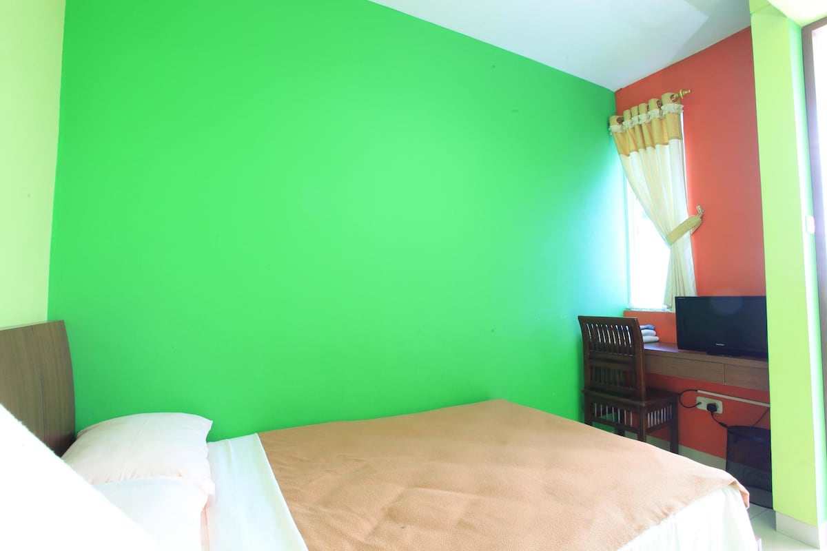 A room with a bed, a desk with a chair, and a television.